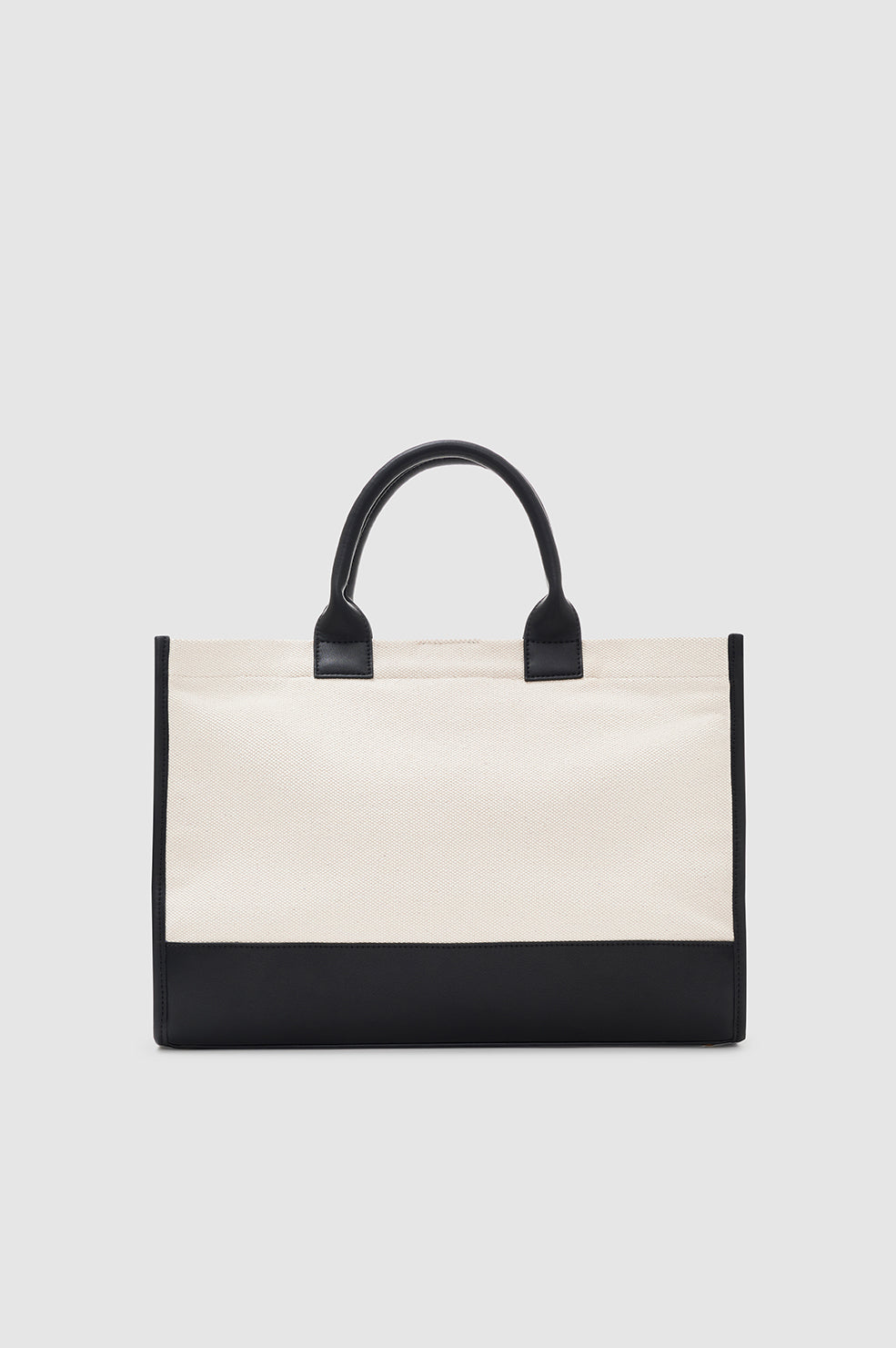 The Anine Bing Medium Lara Tote features a cream cotton canvas body with black leather trim and handles, shown against a simple light background.