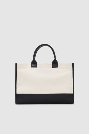 The Anine Bing Medium Lara Tote features a cream cotton canvas body with black leather trim and handles, shown against a simple light background.