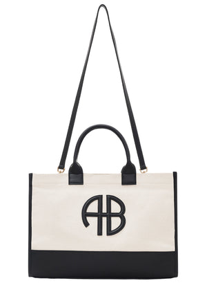 The Medium Lara Tote by Anine Bing is a rectangular beige cotton canvas bag with black handles, a long shoulder strap, leather accents, black trim, and a bold "AB" monogram on the front.