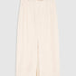 The Meredith Skirt by Anine Bing, a beige knee-length tailored piece featuring a front slit, belt loops, and side pockets, is displayed flat against a plain grey background.