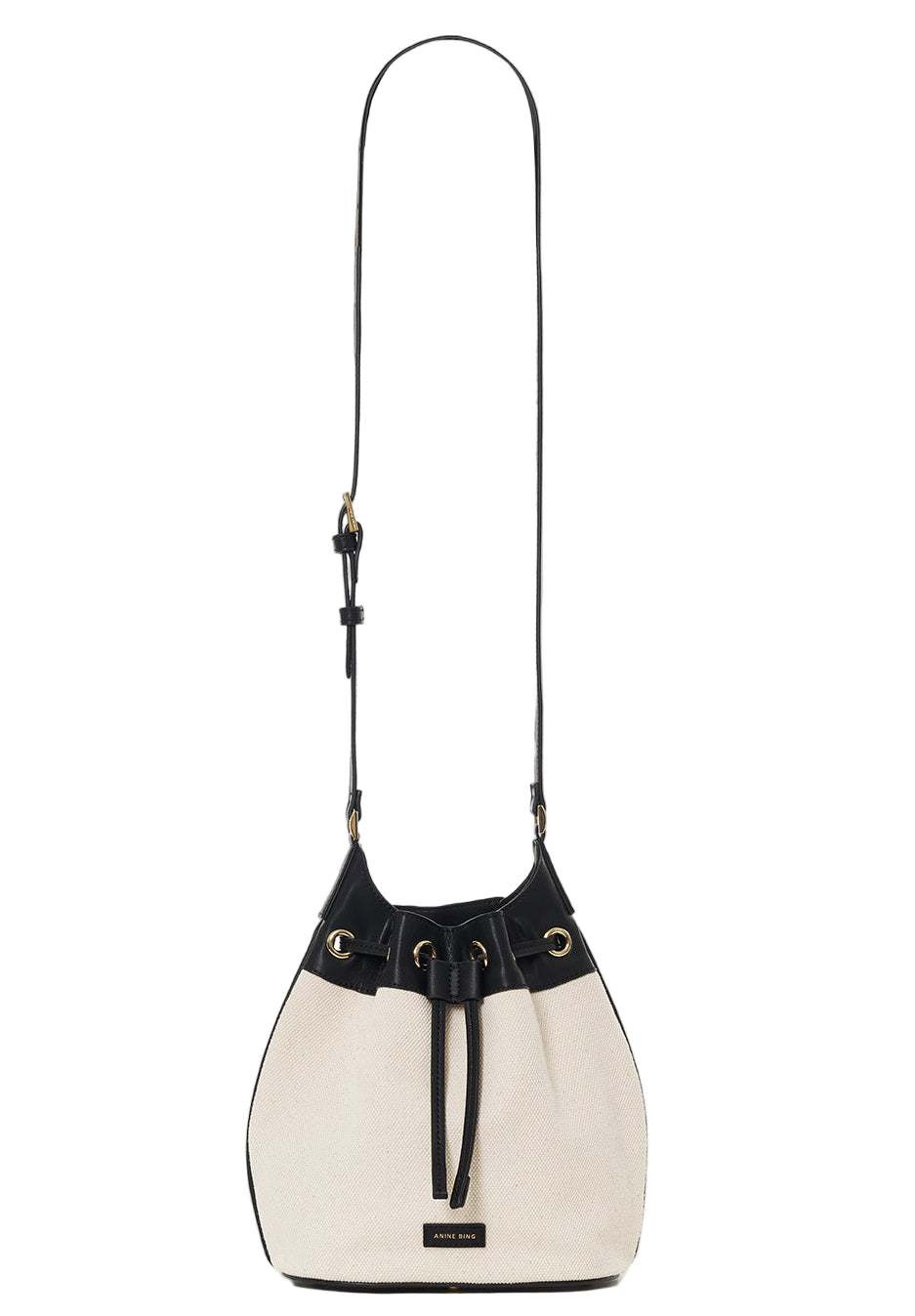 The Mini Alana Bucket Bag by Anine Bing features a cream and black design, drawstring closure, gold-tone hardware, adjustable shoulder strap, and a small rectangular front label.