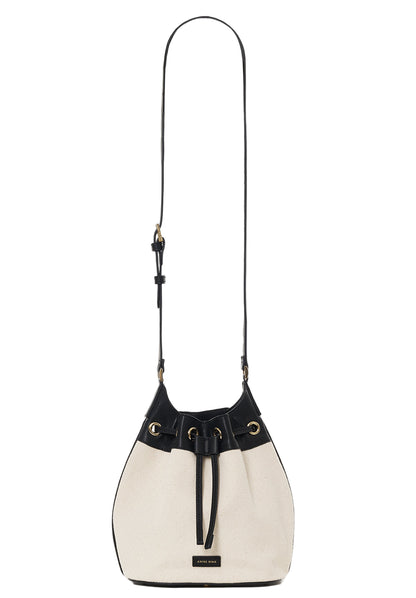 The Mini Alana Bucket Bag by Anine Bing features a cream and black design, drawstring closure, gold-tone hardware, adjustable shoulder strap, and a small rectangular front label.