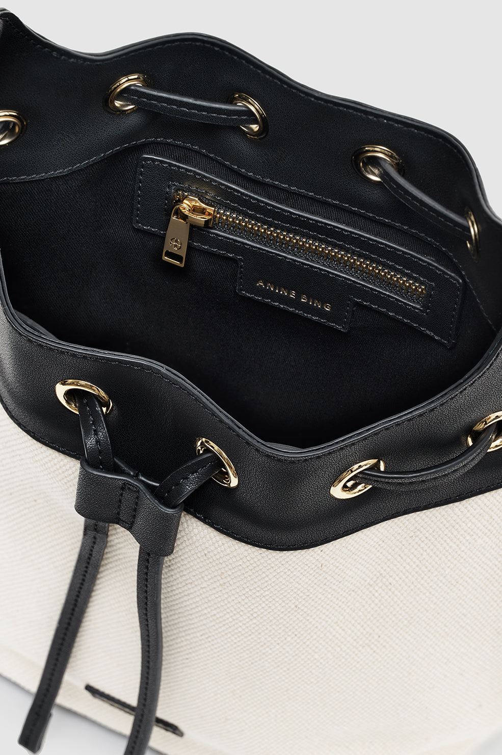 A close-up of the Mini Alana Bucket Bag’s interior reveals a black zippered pocket with gold-tone hardware and “Anine Bing” branding on the lining.