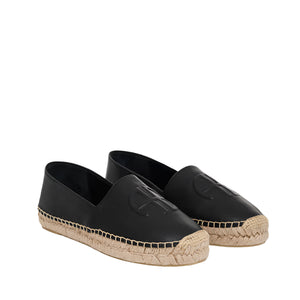 The Paloma Espadrilles by Anine Bing feature black leather, a woven jute sole, and an embossed monogram on the upper, offering a chic yet timeless appeal.