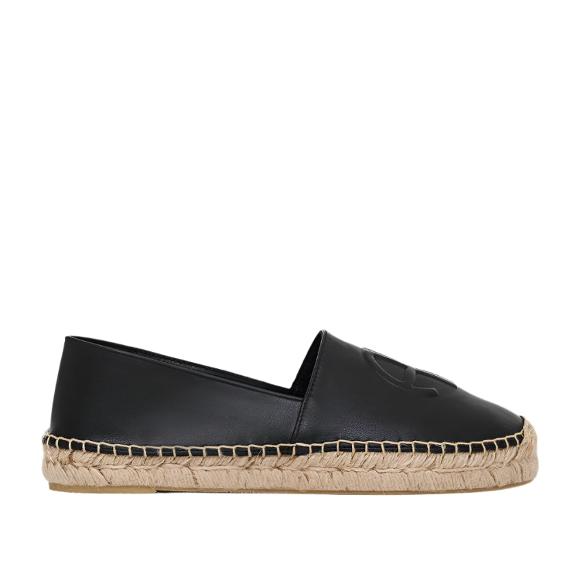The Paloma Espadrilles from Anine Bing feature a sleek black leather finish with a woven jute sole and an embossed front monogram, combining elegance with comfort in a classic slip-on design.