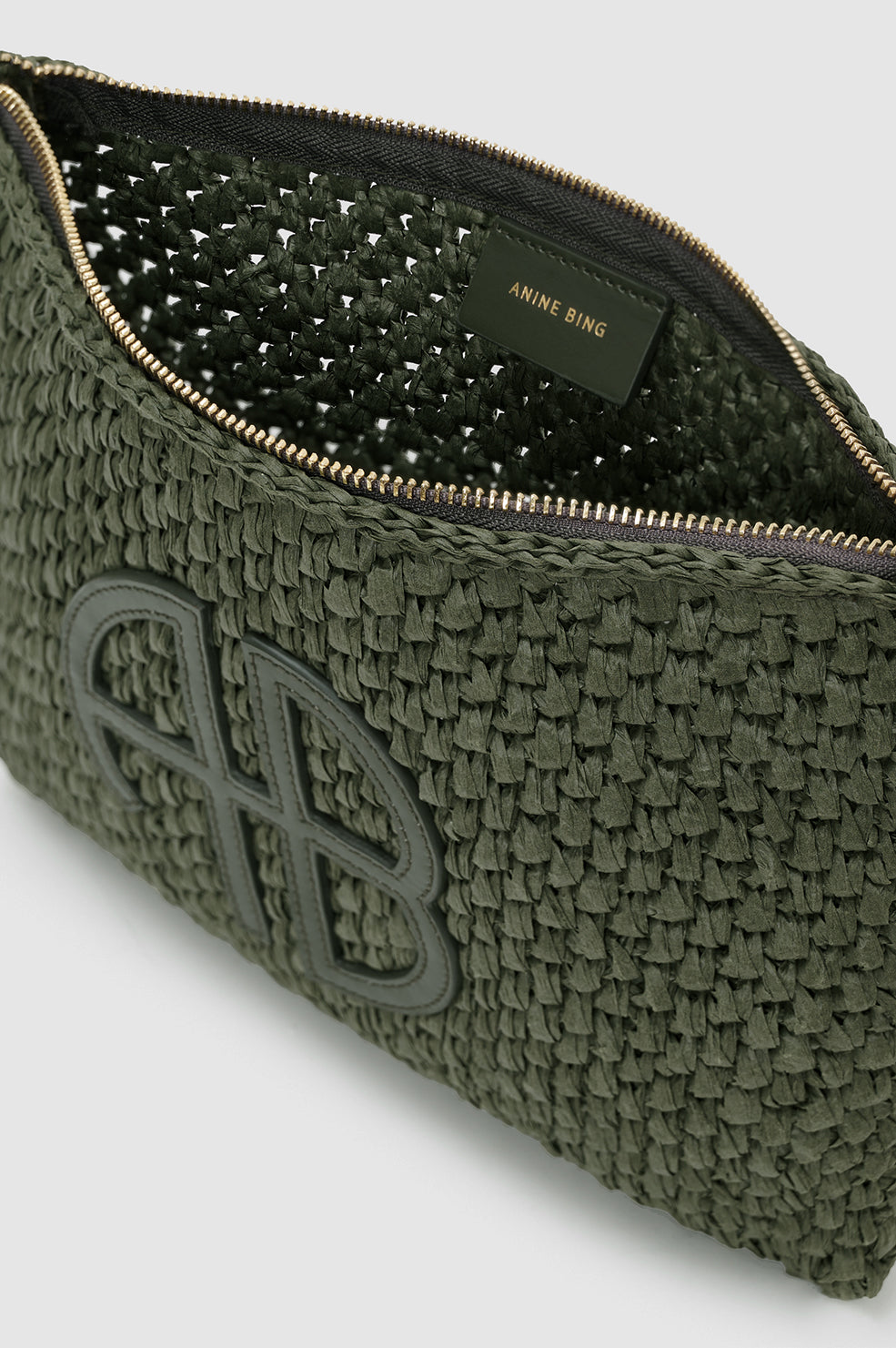 A close-up of the olive green Rio Woven Pouch by Anine Bing, open to reveal a zipper and "ANINE BING" label inside. The exterior features a raised logo design.