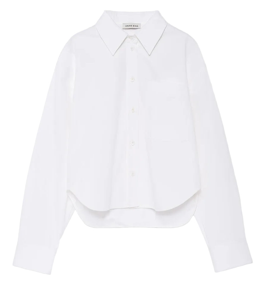 The Scott Cropped Shirt by Anine Bing is a white long-sleeve button-up featuring a collar, chest pocket, and subtly curved hem. Made from crisp cotton poplin for comfortable wear, it boasts a relaxed silhouette and is showcased against a plain white background.