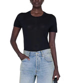 Model wearing the Anine Bing Sylvie Tee, a fitted black super soft crewneck top, paired with light blue high-waisted jeans, standing against a white background.