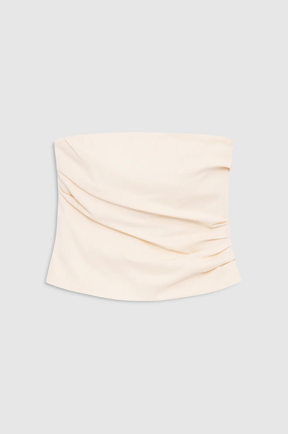 The Tyla Top by Anine Bing is a beige, strapless bandeau featuring subtle ruched detailing on one side and displayed against a plain gray background. With its sculpted shape that flatters the silhouette, this versatile top is a chic addition to any wardrobe.