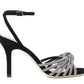 Loeffler Randall Ada Black Knot Heeled Sandal by Loeffler Randall is a black suede high-heeled sandal featuring an ankle strap adorned with decorative silver bead embellishments and sparkling rhinestones.