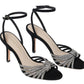 A pair of black suede high-heeled sandals with ankle straps and rhinestone detailing on the front, named "Loeffler Randall Ada Black Knot Heeled Sandal," featuring the "Loeffler Randall" label on the insole.