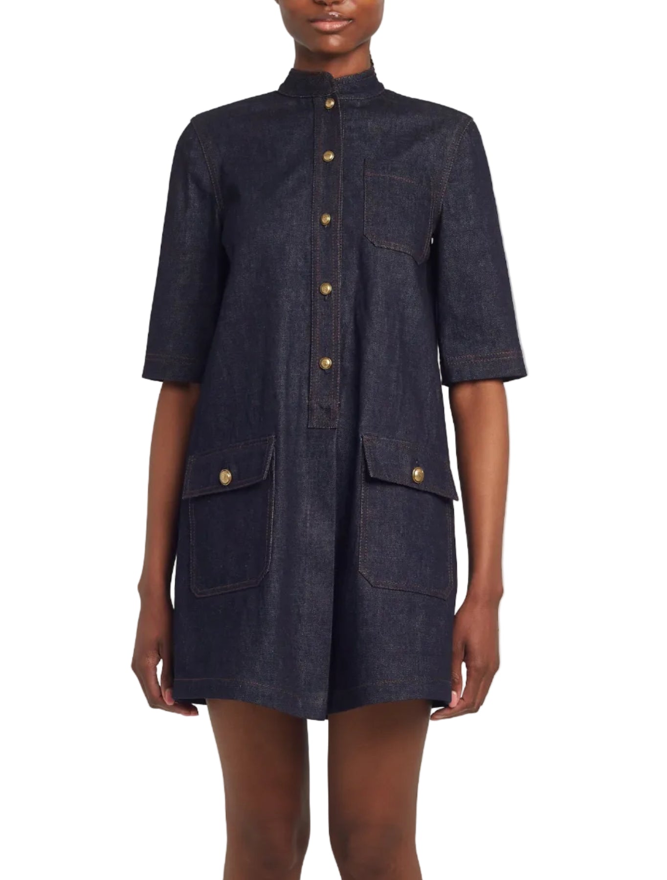 A person wears the Adam Lippes Lauder Dress, a short-sleeve dark Japanese indigo denim button-up with three front pockets, antique gold buttons, and subtle topstitching, standing against a white background.