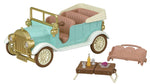 The Calico Critters Classic Family Car is a charming toy vehicle in pastel colors, complete with removable seats—including seating for up to 10 figures—and delightful accessories like a picnic table, two glasses, two bottles, and a plate with food, all beautifully presented against a white background.