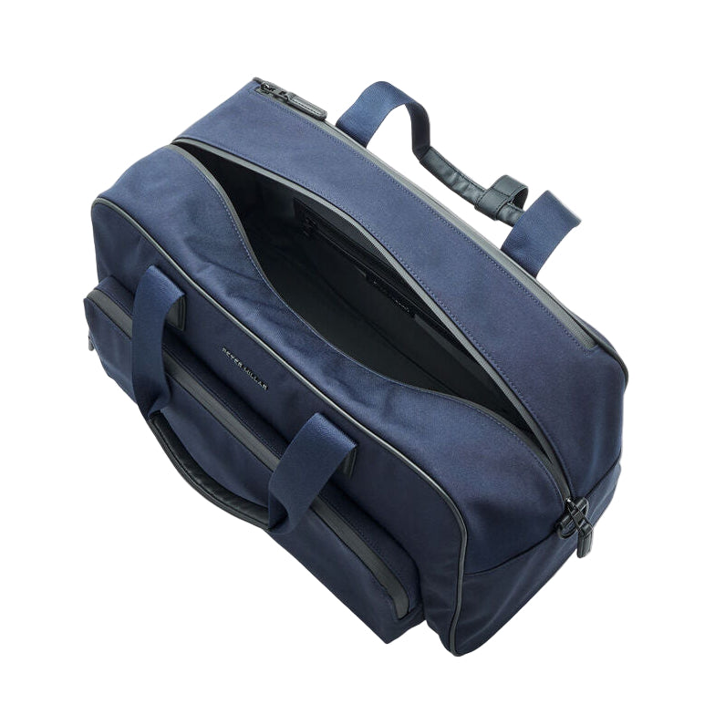A navy blue Peter Millar Pursuit Duffle with black handles and zippers is shown partially unzipped, revealing its main compartment and interior pockets.