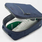 The Peter Millar Pursuit Shoe Bag in navy, featuring genuine leather trim and a zippered closure, is shown partially open to reveal white sneakers with green accents against a white background.