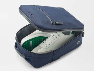 The Peter Millar Pursuit Shoe Bag in navy, featuring genuine leather trim and a zippered closure, is shown partially open to reveal white sneakers with green accents against a white background.