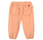 The Cozmo Baby Girls’ Agen Corduroy Pants feature a peach-colored micro-corduroy fabric, an elastic waist and cuffs, two ruffled back pockets, and a small embroidered red flower above the right pocket.