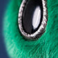 Close-up of a shiny black and silver eye on galactic green fuzz, likely part of the Jellycat Zyllan Alien plush toy.