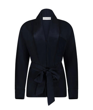The Alba Blouse by Victoria Beckham is a black long-sleeve top with a shawl collar and matching fabric belt tied at the waist, featuring an elegant drape, displayed on a plain white background.