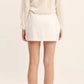 A person stands facing away, wearing a long-sleeved cream top, beige shoes, and the white linen Alice Skirt with an A-line silhouette by POSSE.