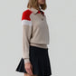A woman wears the Guest in Residence Alpine Collegiate Polo, featuring red and white shoulder accents, paired with a pleated black skirt, standing against a plain light gray background.