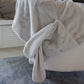 A Bloom Tuck Me in Blanket by Bunnies By the Bay, featuring an adorable plush bunny design with long ears and a stitched face, adorns this soft gray fleece draped over a chair—perfect for a baby shower gift.