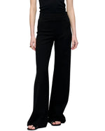 Model wears the Anouk Pant by Callas Milano, featuring a high-waisted, wide-leg crepe jersey design, paired with a sleeveless black top against a plain white background.
