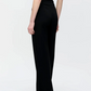 A person stands facing away, wearing Callas Milano's Anouk Pant in black crepe jersey and a sleeveless black top against a plain light background.