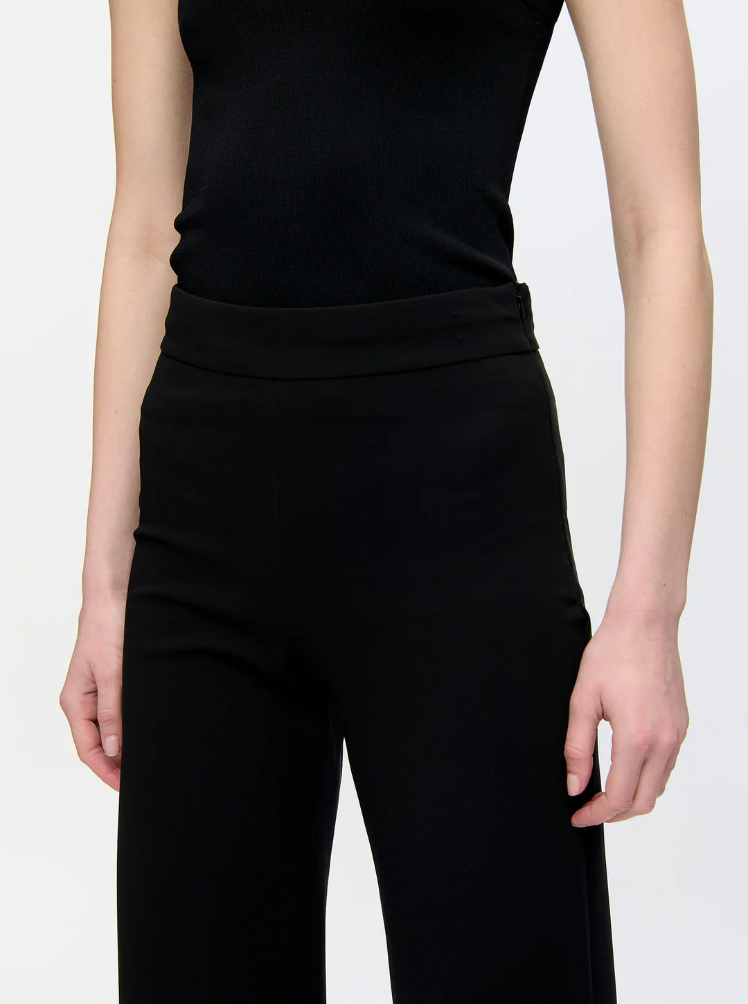 A person wears the Callas Milano Anouk Pant, a high-waisted travel pant, paired with a sleeveless black top. They are shown from shoulders to mid-thigh against a plain background.