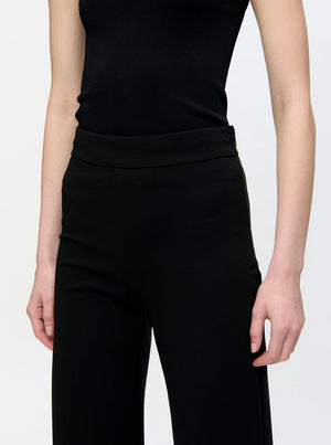 A person wears the Callas Milano Anouk Pant, a high-waisted travel pant, paired with a sleeveless black top. They are shown from shoulders to mid-thigh against a plain background.