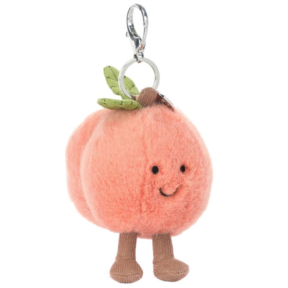 The Jellycat Amuseables Peach Bag Charm features a smiling face, green leaf accents, and brown legs on a plush peach, attached to a metal keyring and clip—perfect for adding cute charm to any bag.