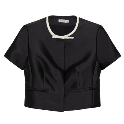 Simkhai Naelle Top in structured black satin, featuring a cropped short-sleeve silhouette, white crew neckline, and a small decorative bow at the center.