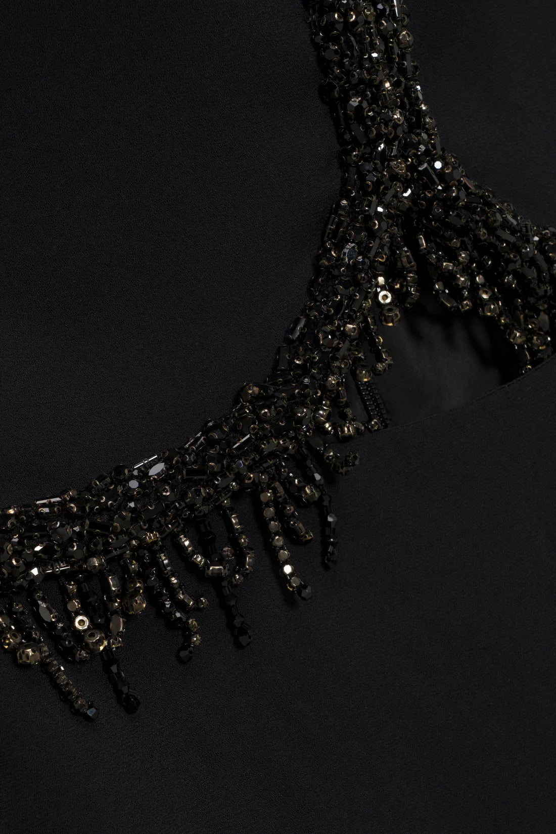 Close-up of the Simkhai Zoriel Gown, featuring a black crepe neckline embellished with dark beads and hanging crystal fringe.