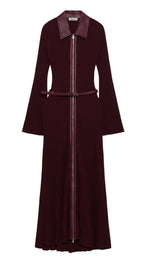 Simkhai’s Ismelle Midi Dress features long sleeves, a wide collar, a front zipper, flared cuffs, and a ribbed knit texture throughout the skirt. The dress comes in burgundy and includes a matching leather belt at the waist.
