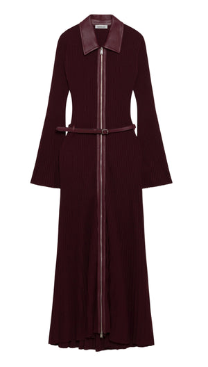 Simkhai’s Ismelle Midi Dress features long sleeves, a wide collar, a front zipper, flared cuffs, and a ribbed knit texture throughout the skirt. The dress comes in burgundy and includes a matching leather belt at the waist.