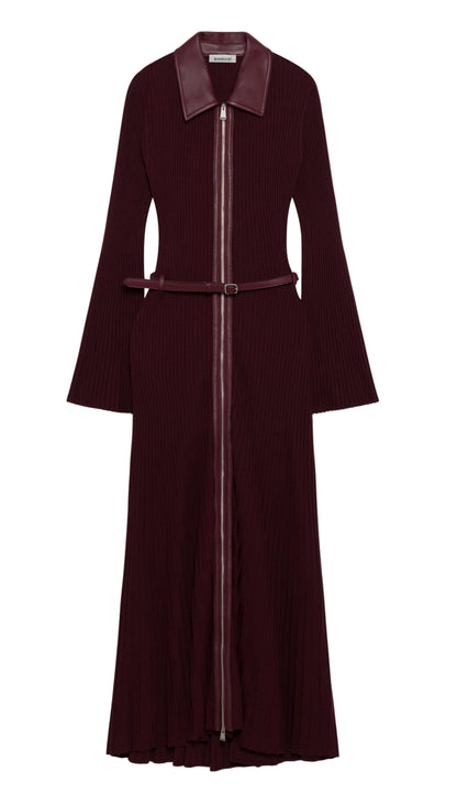 Simkhai’s Ismelle Midi Dress features long sleeves, a wide collar, a front zipper, flared cuffs, and a ribbed knit texture throughout the skirt. The dress comes in burgundy and includes a matching leather belt at the waist.