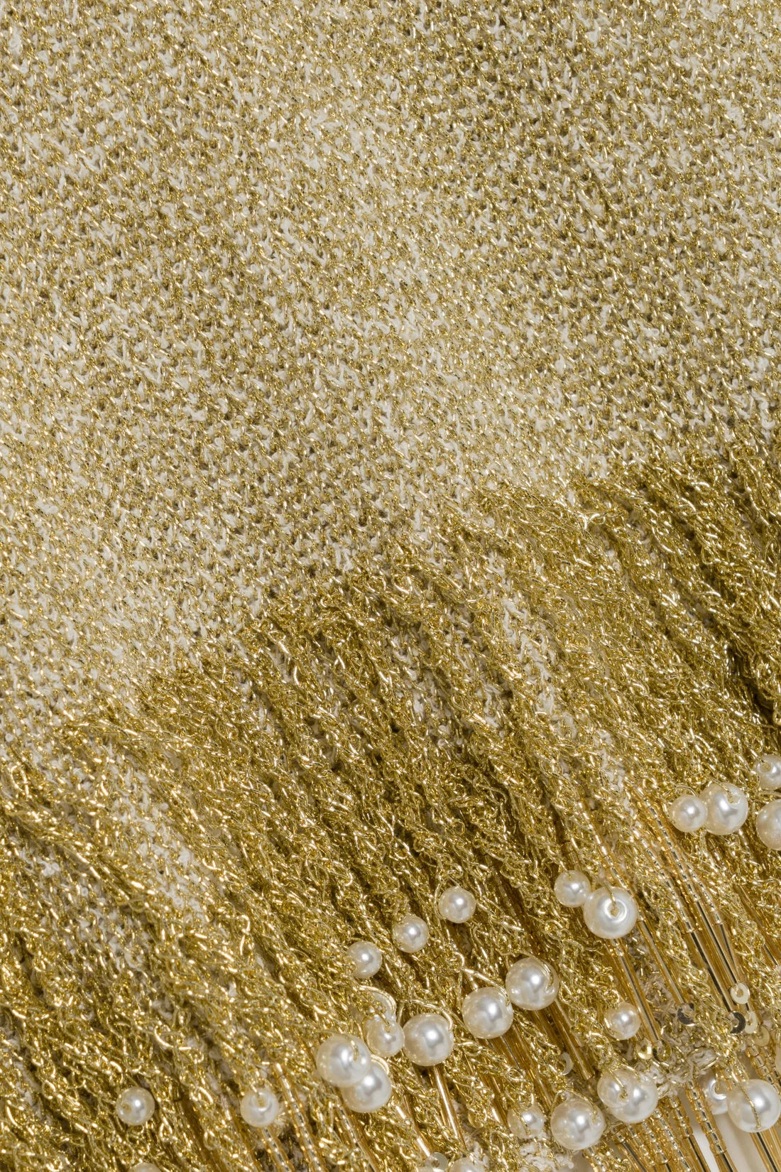 Close-up of the Simkhai Tali Pearl Fringe Top, a metallic gold bouclé knit fabric featuring long gold fringe embellished with round white pearls.