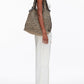 A person in a white sleeveless top and white pants stands in profile, carrying the 3.1 Phillip Lim Crochet Raffia Market Tote over their shoulder.