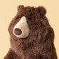 Jellycat Bizzlestomp Bear plush brown stuffed animal with a cream snout and black nose, shown on a plain beige background.