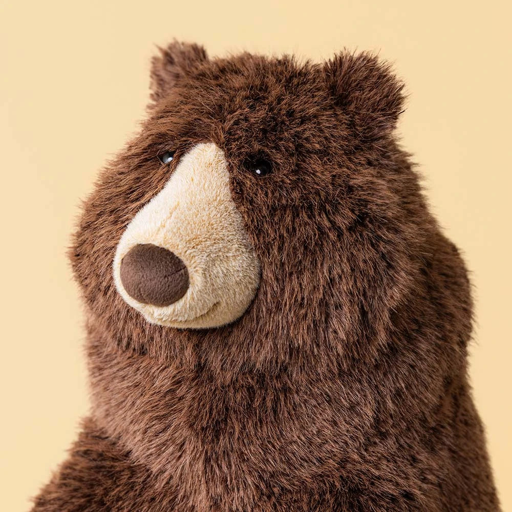 Jellycat Bizzlestomp Bear plush brown stuffed animal with a cream snout and black nose, shown on a plain beige background.