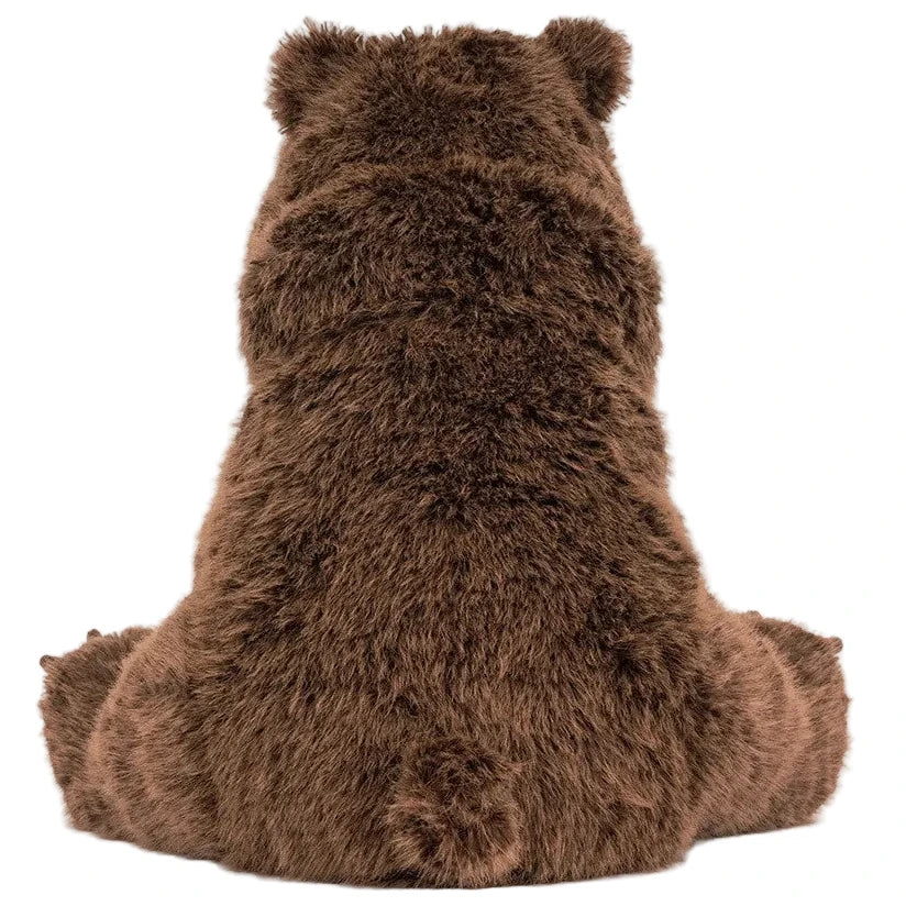 The large brown Bizzlestomp Bear by Jellycat sits with its back to the viewer, highlighting its fluffy fur and signature round ears.