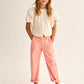 A young girl stands with her hands in her pockets, wearing a white ruffled blouse, Cozmo Girls' Atena Pants featuring a classic twill design and elastic waistband, paired with pink flats against a neutral background.