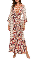 A woman wears the Figue Athena Dress, a long, patterned wrap style with a tie belt, showcasing red, orange, and black designs on a cream background.