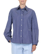 A person is wearing the Aura Top by Callas Milano, a blue and white Italian stripe poplin button-up shirt, paired with light blue pants against a plain white background.