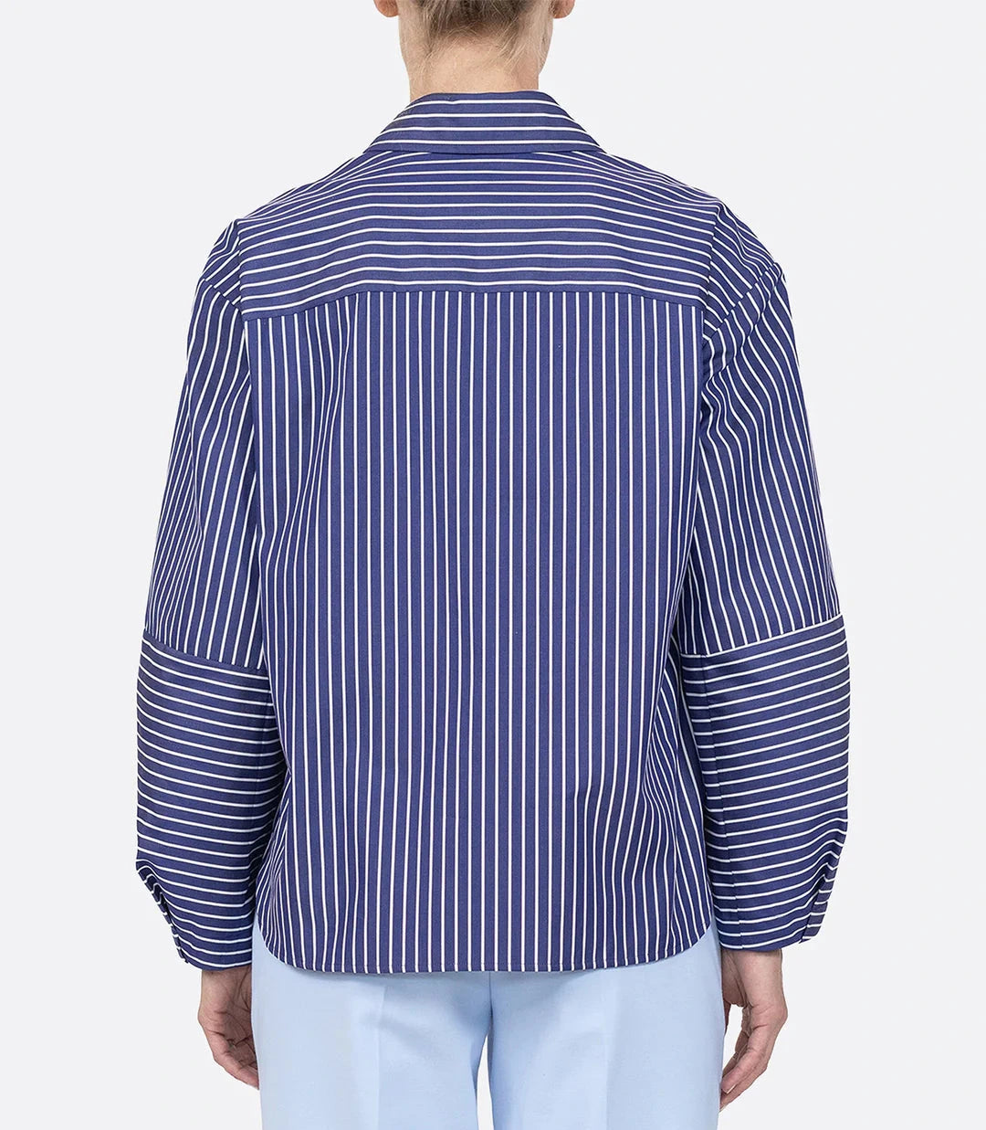 Person wearing the Aura Top by Callas Milano, a blue and white Italian stripe poplin long-sleeve shirt featuring horizontal stripes on the upper back and forearms, shown from the back.