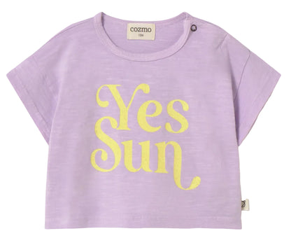 The Cozmo Baby Girls' Aura T-Shirt is a lightweight cotton top in light purple, featuring a bold yellow "Yes Sun" print on the front and a button detail on the left shoulder.