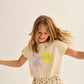 A young girl with long hair, wearing a “feel good day” T-shirt and the Cozmo Girls' Molly Flower Print Skirt, smiles and twirls against a plain light background.
