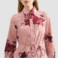 A woman wears the Erdem Long Sleeve Abstract Rose Shirt Dress, a pink cotton poplin button-up with rose bouquets and waist tie, standing against a plain light background.