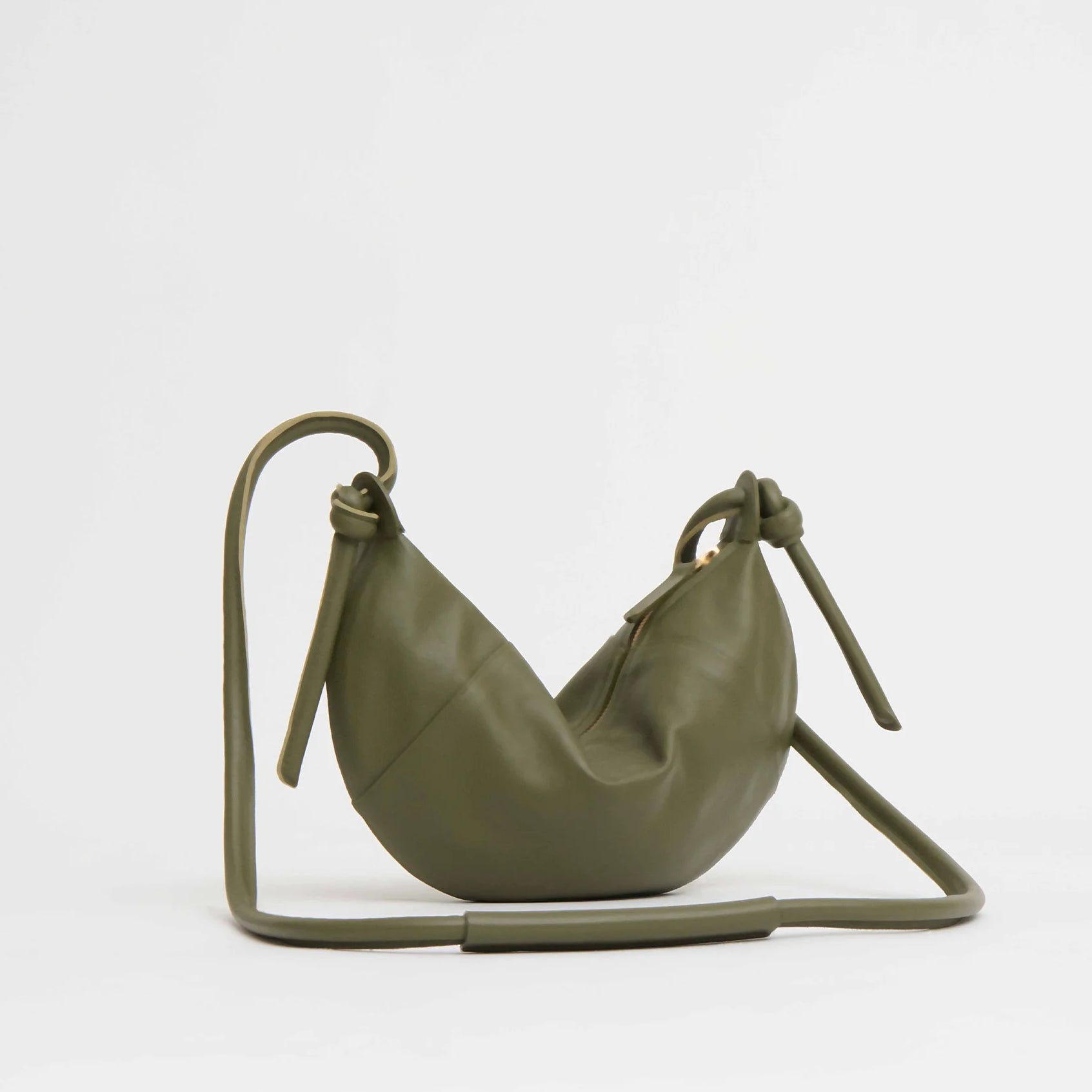 The Mini Fortuna Bag by Mansur Gavriel, made of premium olive green calf leather, features a crescent shape, knotted leather ends, and a long adjustable strap, shown against a plain white background.