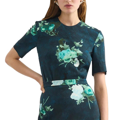 Model in Erdem’s Short Sleeve Abstract Rose Top, featuring dark blue fabric with green and white abstract roses, short sleeves, and a fitted waist; shown from shoulders to mid-thigh.